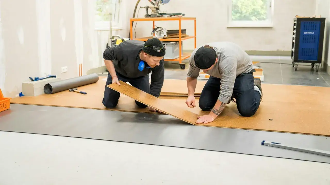 Zwei Männer verlegen kork im badezimmer. Sie knien und fügen die Korkplatten zusammen.