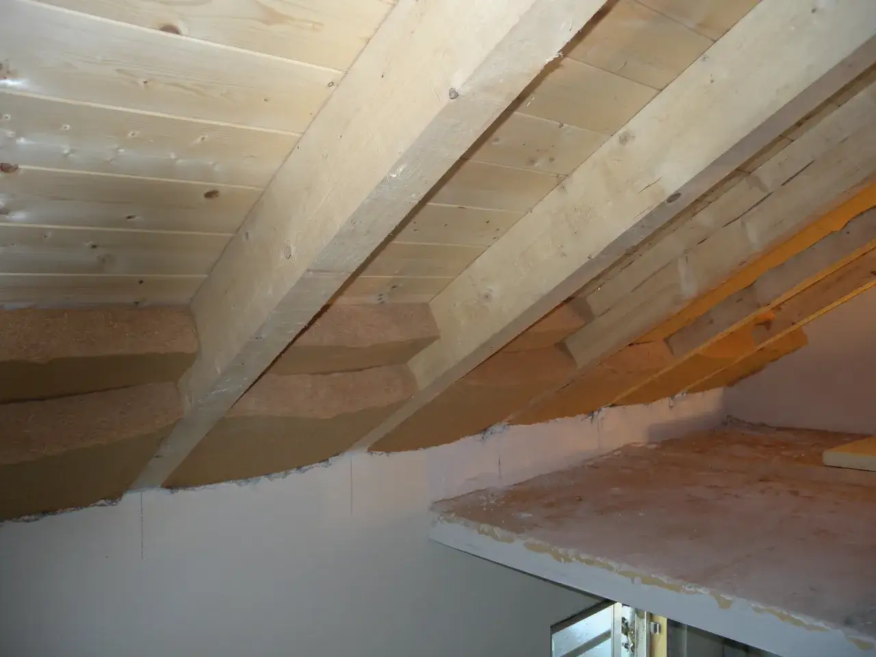 Soffitto a vista con travi in legno e pannelli isolanti in fibra di legno. L'isolamento &egrave; posizionato tra le travi per un soffitto a vista efficiente.