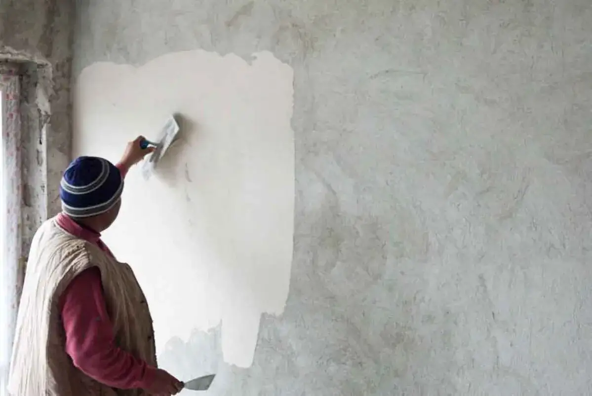 Un ouvrier applique un corps d'enduit chaux sur un mur brut avec une truelle. La texture naturelle de l'enduit est visible.