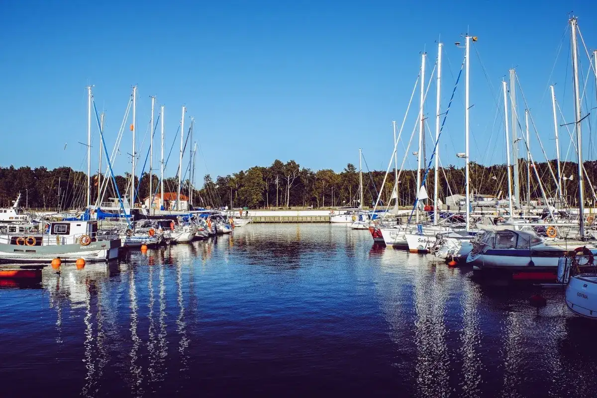 Port jachtowy w Łebie, z wieloma żaglówkami zacumowanymi przy molo.