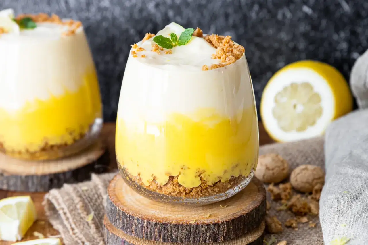 Erfrischendes Dessert im Glas: So einfach kannst du eine Zitronenmelisse Creme selber machen. Mit Keksboden, gelber Creme und wei&szlig;em Topping.