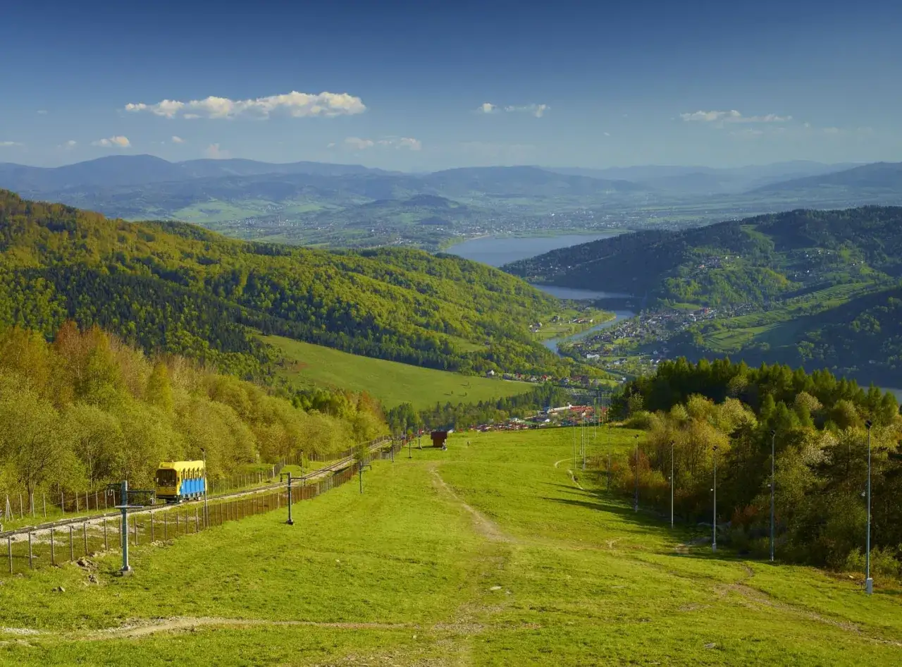 Widok na góry blisko Zatoru, z kolejką górską i jeziorem w oddali.
