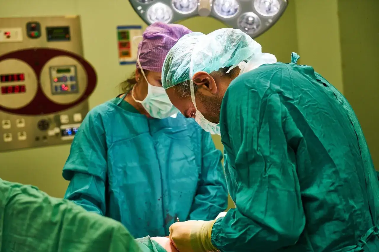 Chirurdzy w maseczkach i czepkach przygotowują się do operacji. Narkoza już działa, pacjent jest bezpieczny.