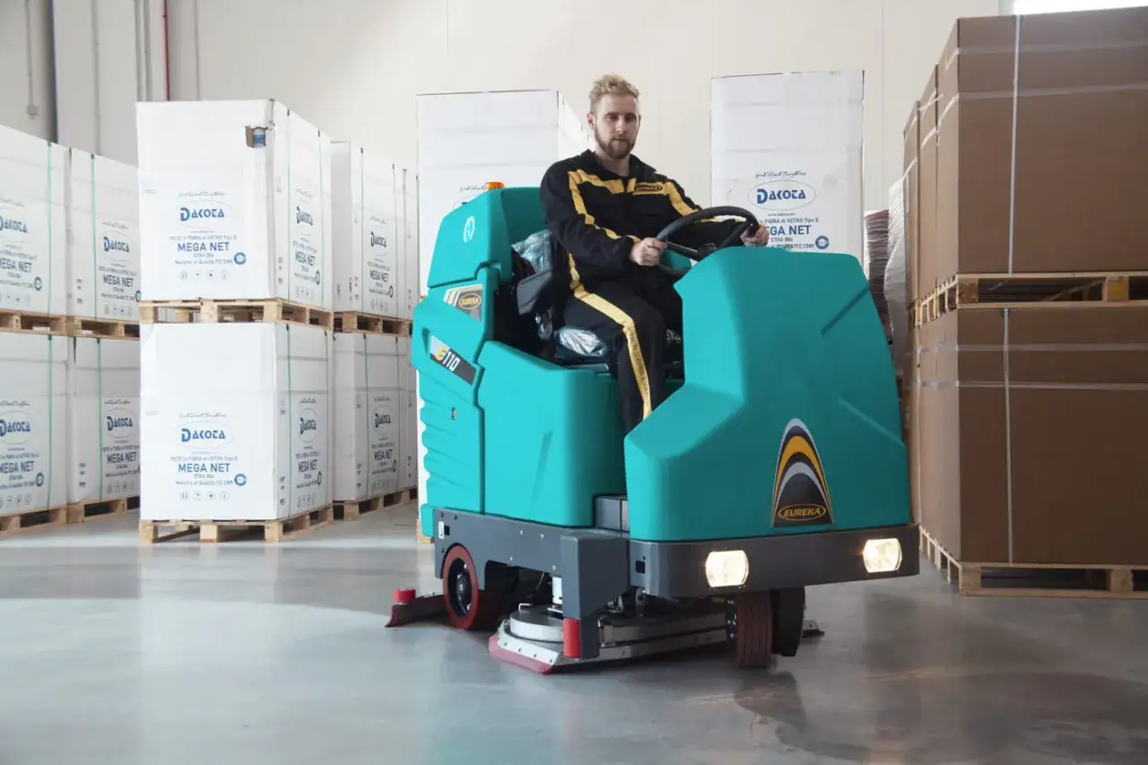 Hombre operando una máquina de limpieza industrial Eureka en un almacén.