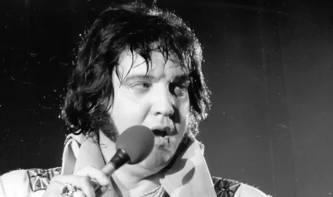 Elvis Presley, sichtlich ersch&ouml;pft, singt ins Mikrofon. Seine Krankheit zeichnet sich ab, doch die Musik lebt weiter.