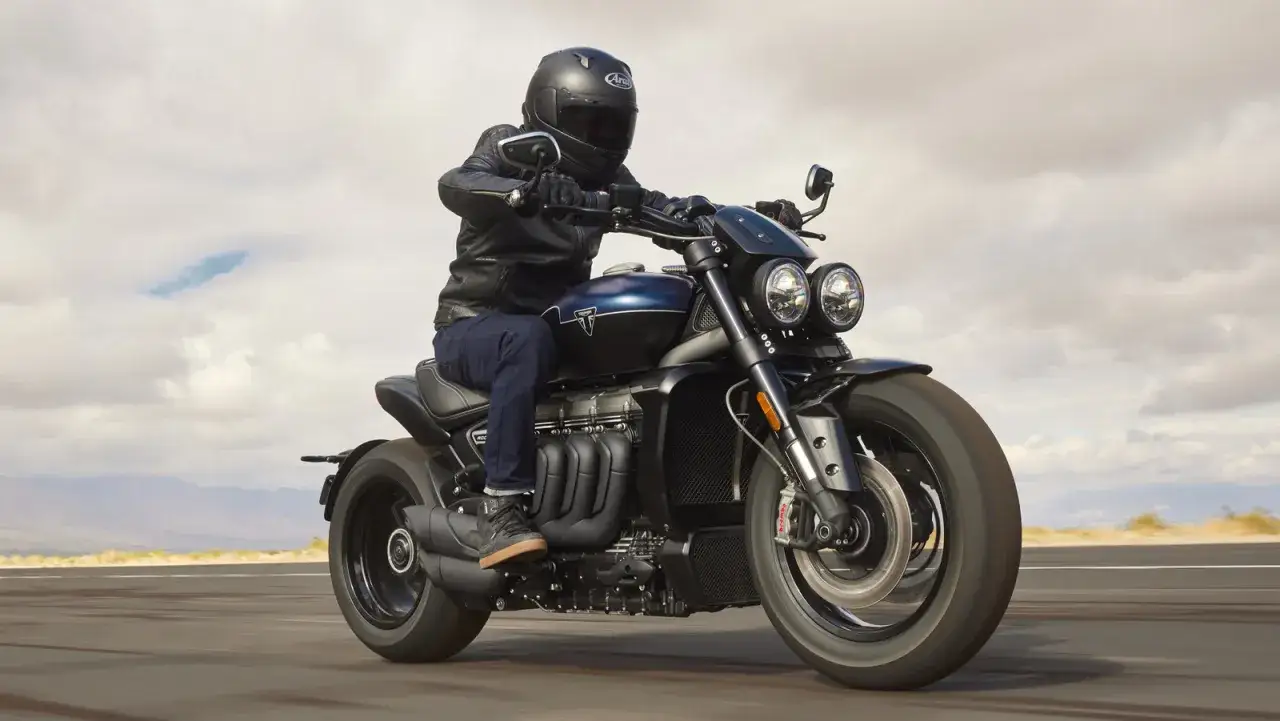 Hombre en moto con mas cc, luciendo chaqueta de cuero y casco, recorriendo una carretera des&eacute;rtica.