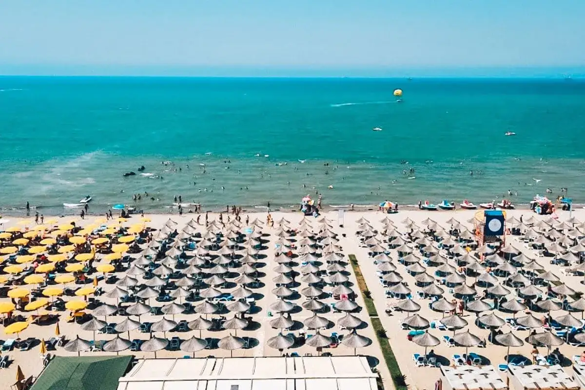 Golem Albania: plaża pełna parasoli i ludzi kąpiących się w turkusowym morzu. Idealne miejsce na wakacje, oferujące liczne atrakcje.