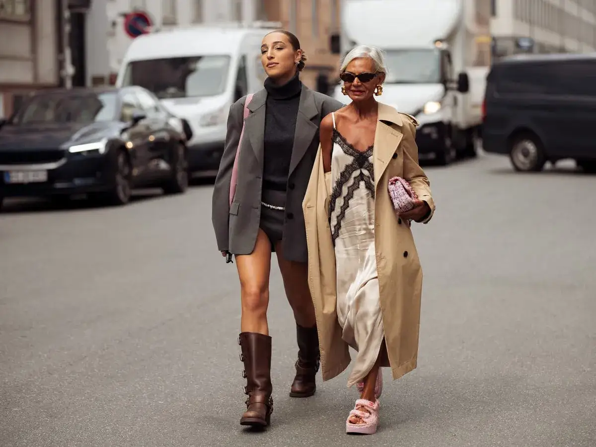 Dos mujeres caminan por la calle. Una lleva un vestido lencero de invierno con un abrigo beige.
