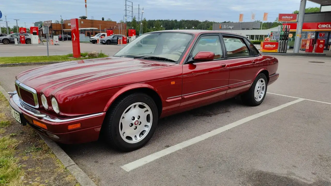 R&ouml;d Jaguar XJ6 till salu, en klassisk sedan med lyxig interi&ouml;r, parkerad vid en bensinstation.