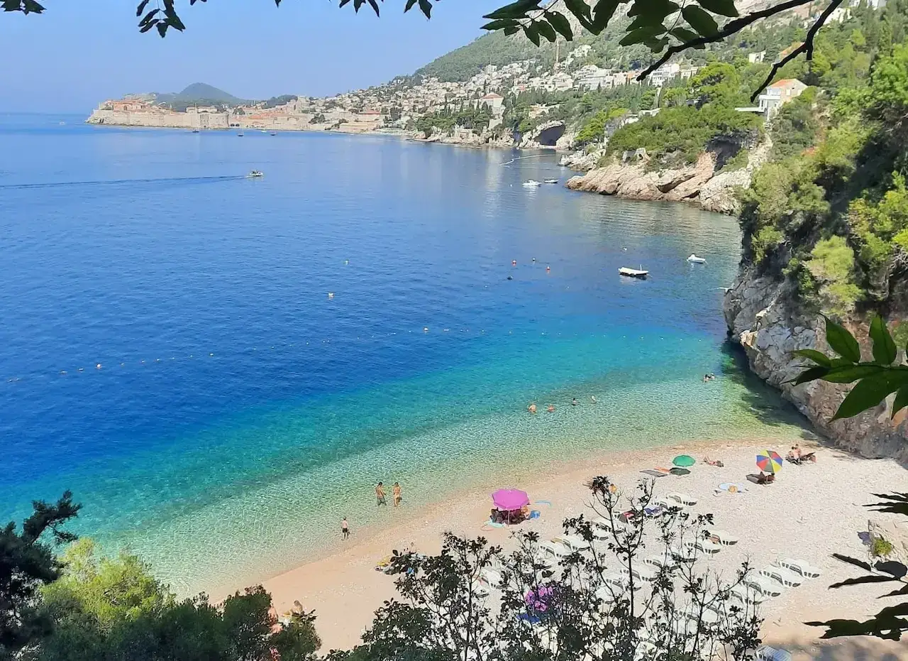 Malownicza zatoka z krystalicznie czystą wodą i kamienistą plażą, idealna na wypoczynek na plażach Dubrownik. W oddali widać zabytkowe miasto.