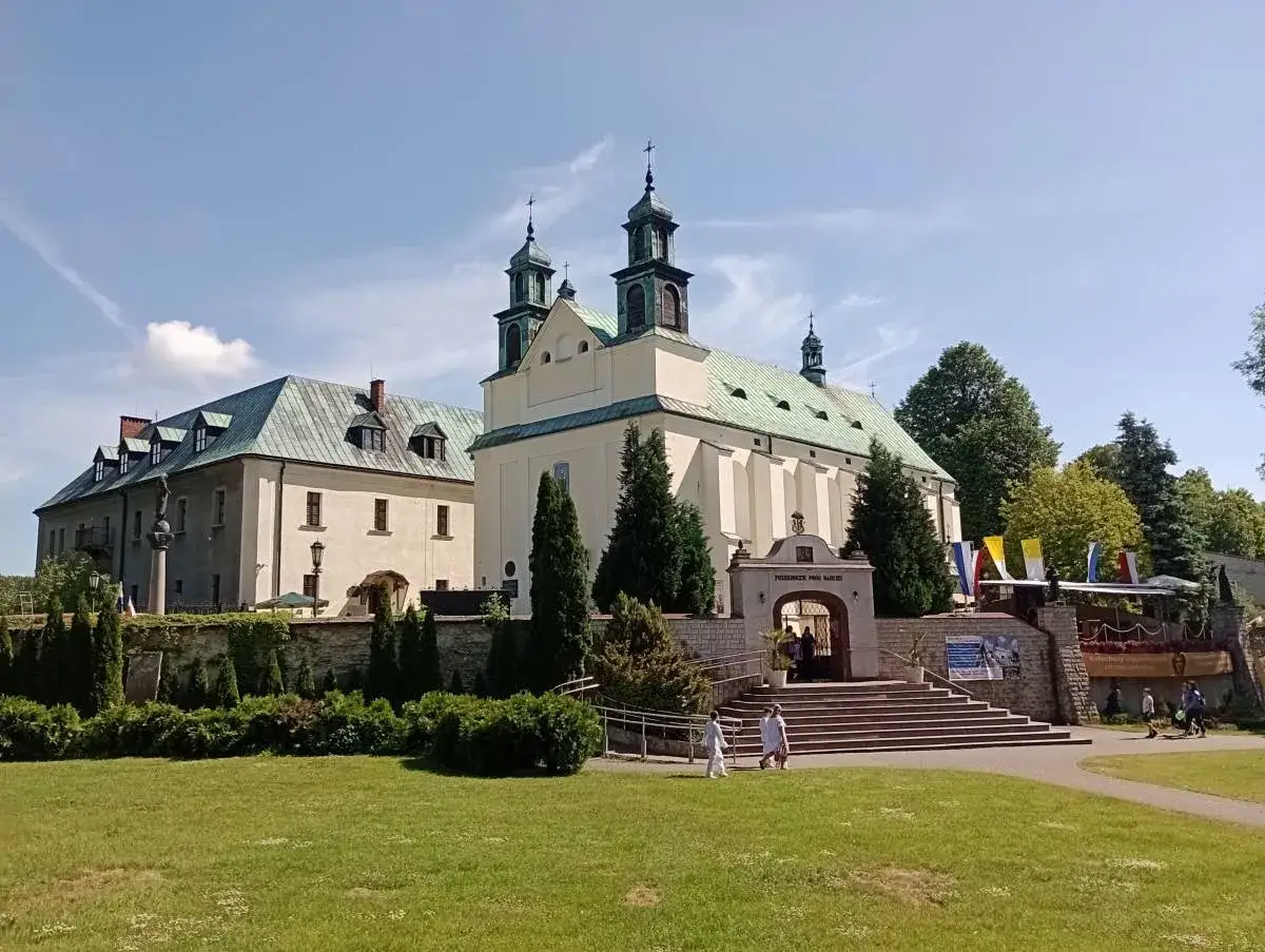 Sanktuarium Matki Boskiej Leśniowskiej z charakterystyczną architekturą i zielonymi dachami, otoczone zadbanym ogrodem.