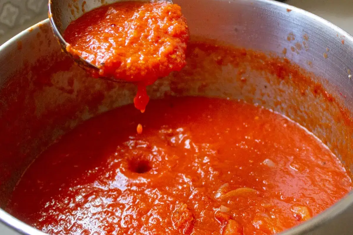 Frisch gekochte Tomatensauce aus San Marzano Tomaten tropft von einer Schöpfkelle in den Topf. Meine besten Tomate San Marzano Erfahrungen!