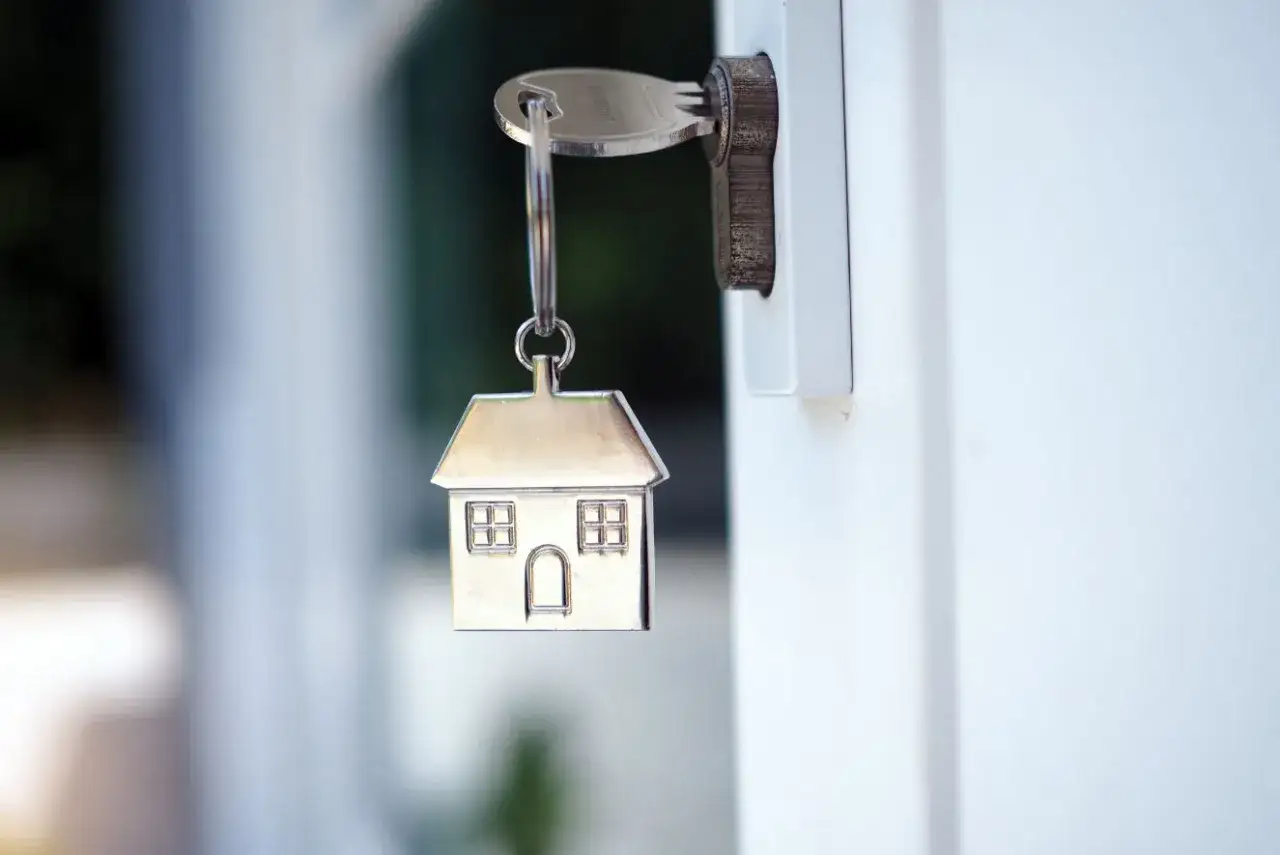 Une cl&eacute; avec un pendentif maison est ins&eacute;r&eacute;e dans une serrure, symbolisant la protection contre le home jacking.