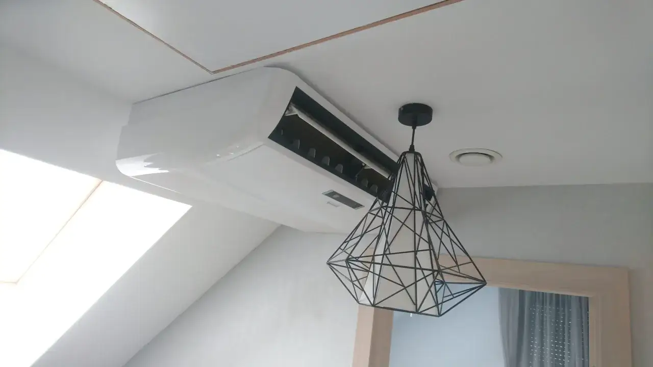Biała klimatyzacja ścienna nad nowoczesną lampą w kształcie diamentu.