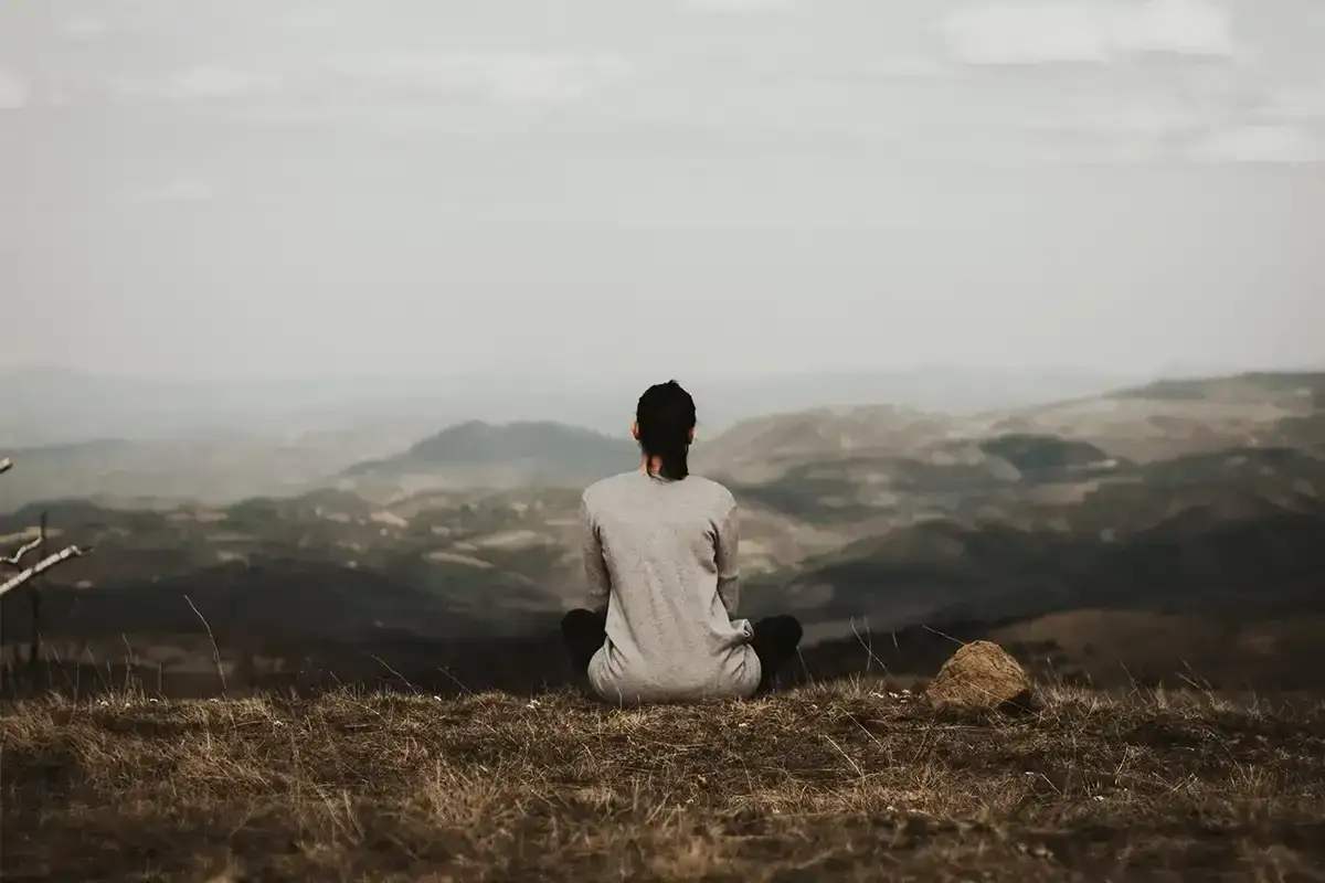 A solitary figure meditates on a hilltop, embodying the spirit of a hermit monk amidst a vast, hazy landscape.
