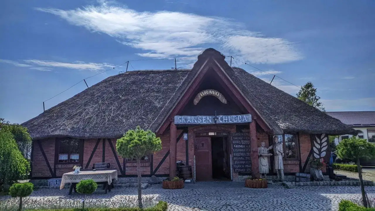 Skansen chleba z charakterystycznym, słomianym dachem. Przed wejściem menu z tradycyjnymi daniami.