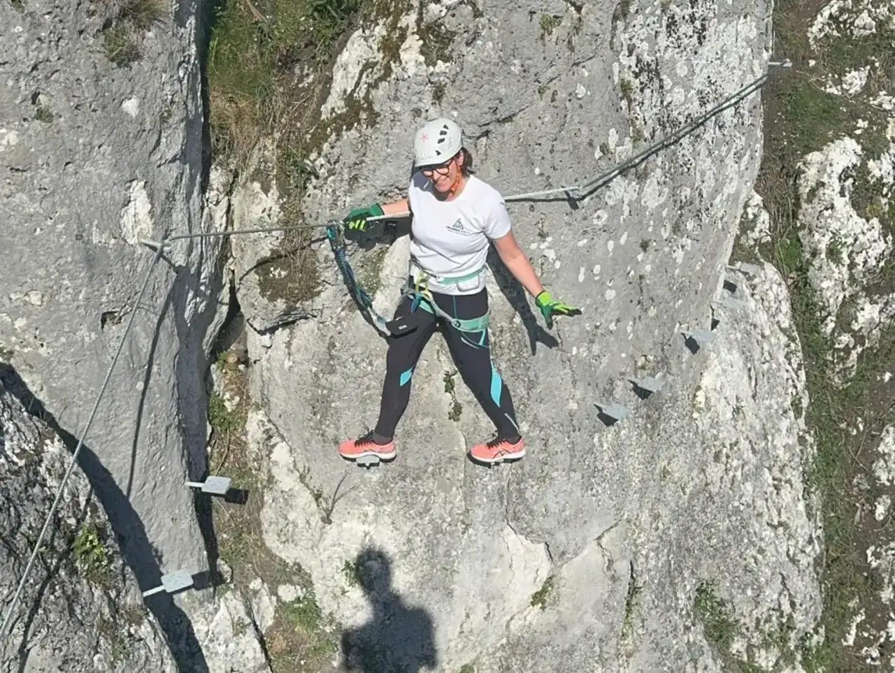 Kobieta w kasku i sprzęcie wspinaczkowym pokonuje via ferrata polska, stawiając kroki na skalnych stopniach.