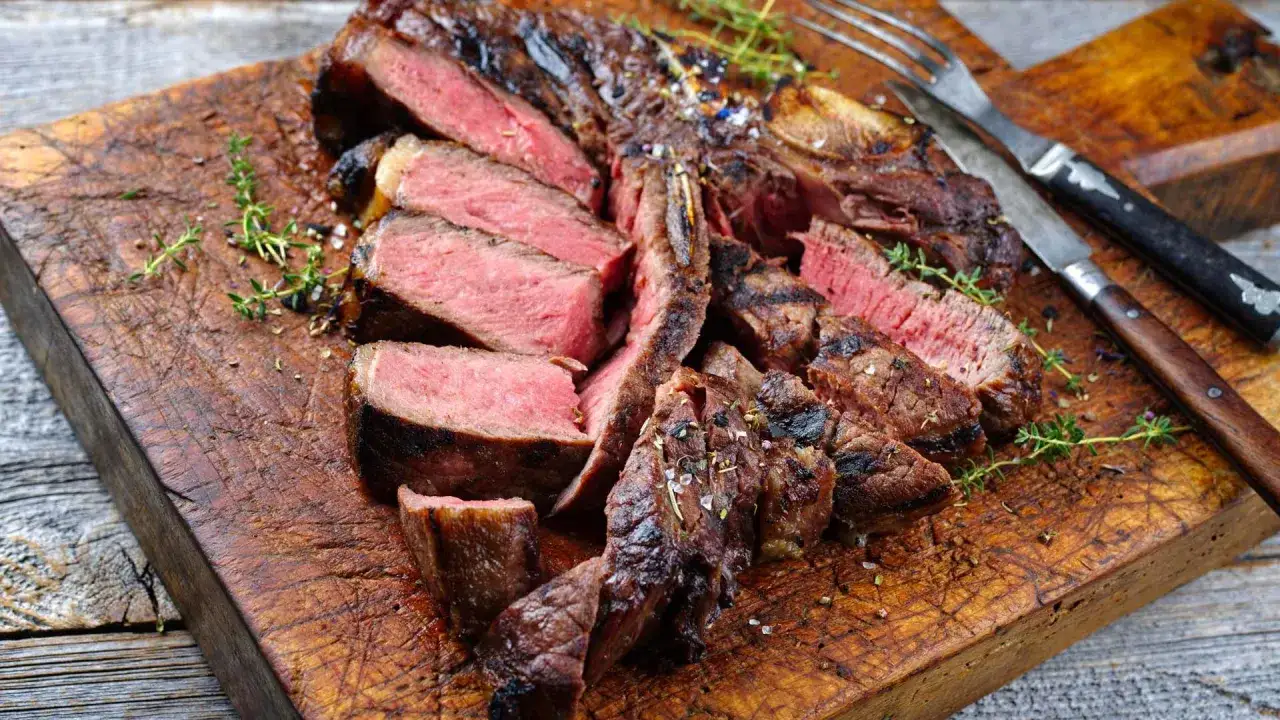 Una succulenta fiorentina steak, affettata e servita su un tagliere di legno, guarnita con erbe aromatiche e sale grosso.