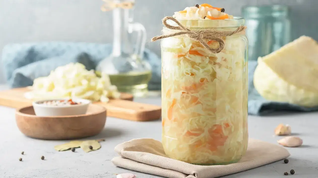 Ein Glas hausgemachtes Sauerkraut, das zeigt, wie gesund Sauerkraut ist. Daneben liegen frische Kohlk&ouml;pfe und Gew&uuml;rze.