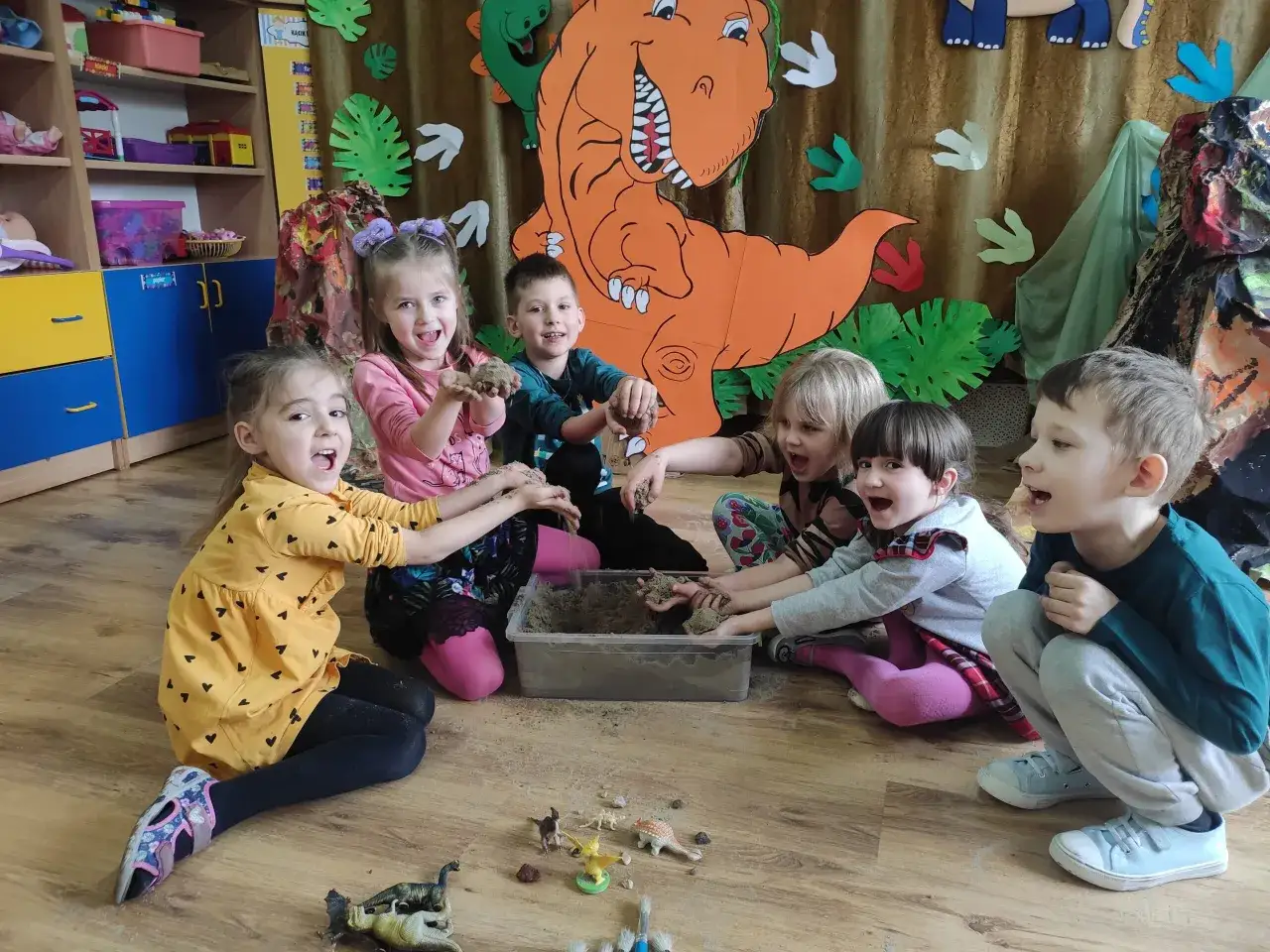 Radosny dzień dinozaura w przedszkolu! Dzieci bawią się piaskiem i figurkami prehistorycznych gadów, tworząc własny świat.