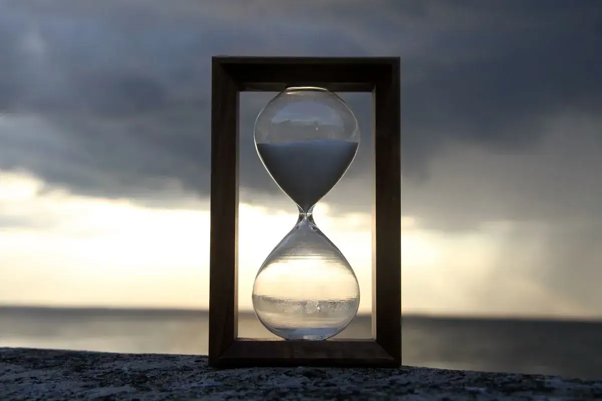 Clessidra con la sabbia del tempo che scorre, sullo sfondo di un mare tempestoso al tramonto.