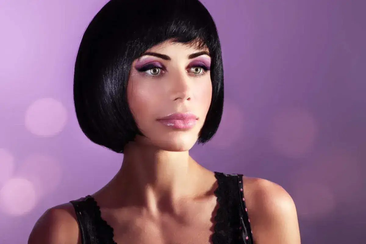 Donna con un elegante caschetto corto pari, trucco viola e labbra lucide, su sfondo sfocato lilla.