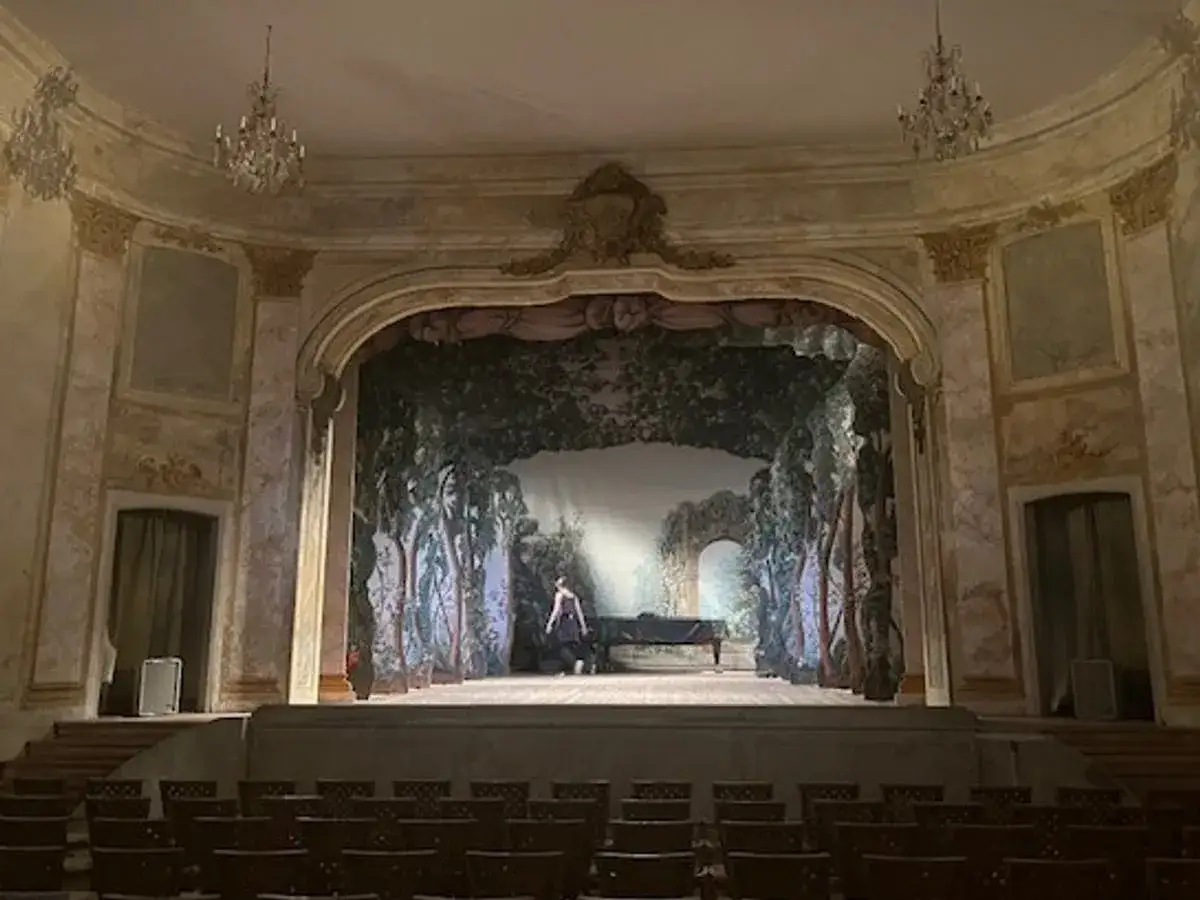 En ensam person vid ett piano på en scen med en skogsmålning, i den anrika Confidencen Ulriksdal.