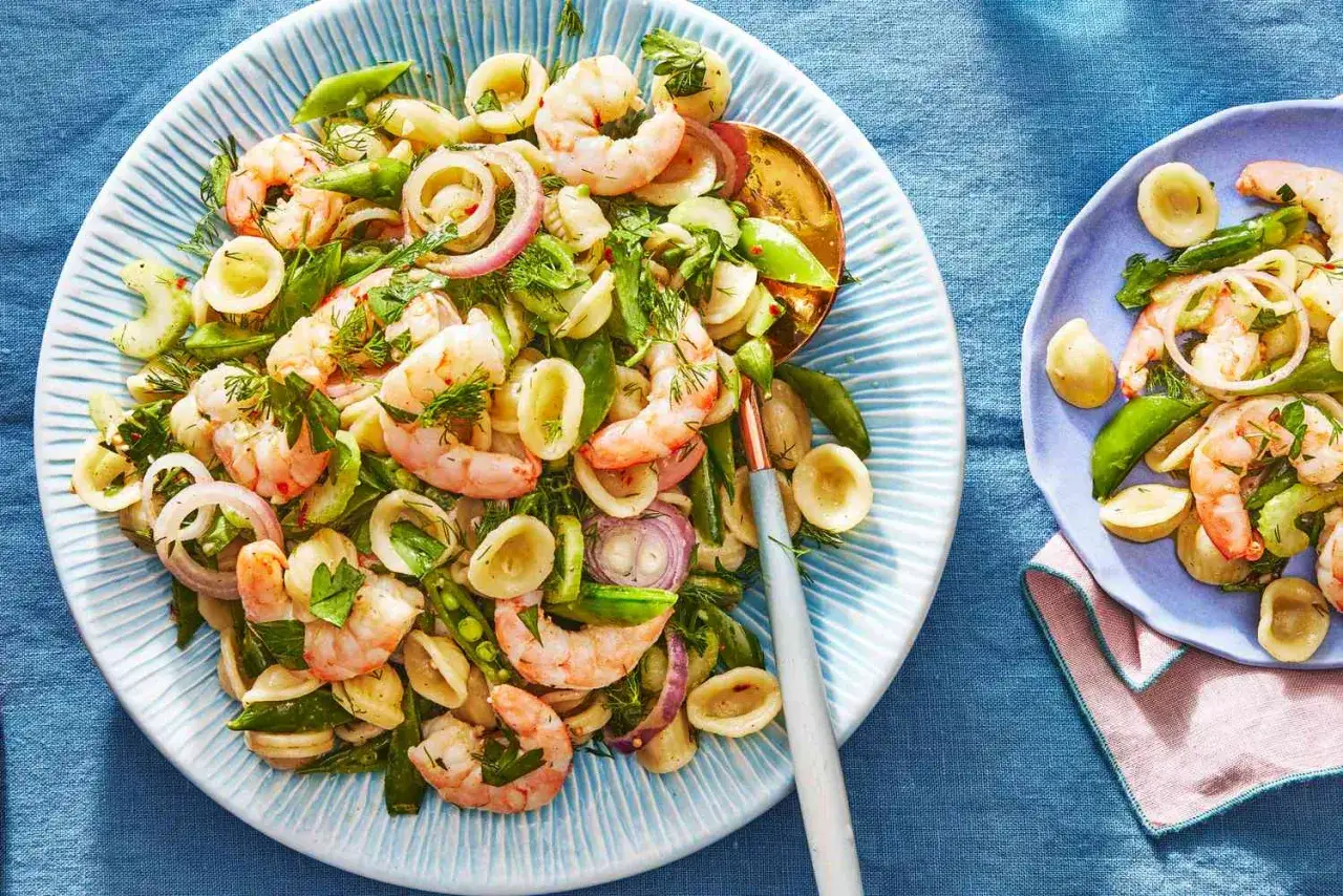 Kolorowe krewetki z warzywami i makaronem orecchiette, udekorowane świeżym koperkiem.