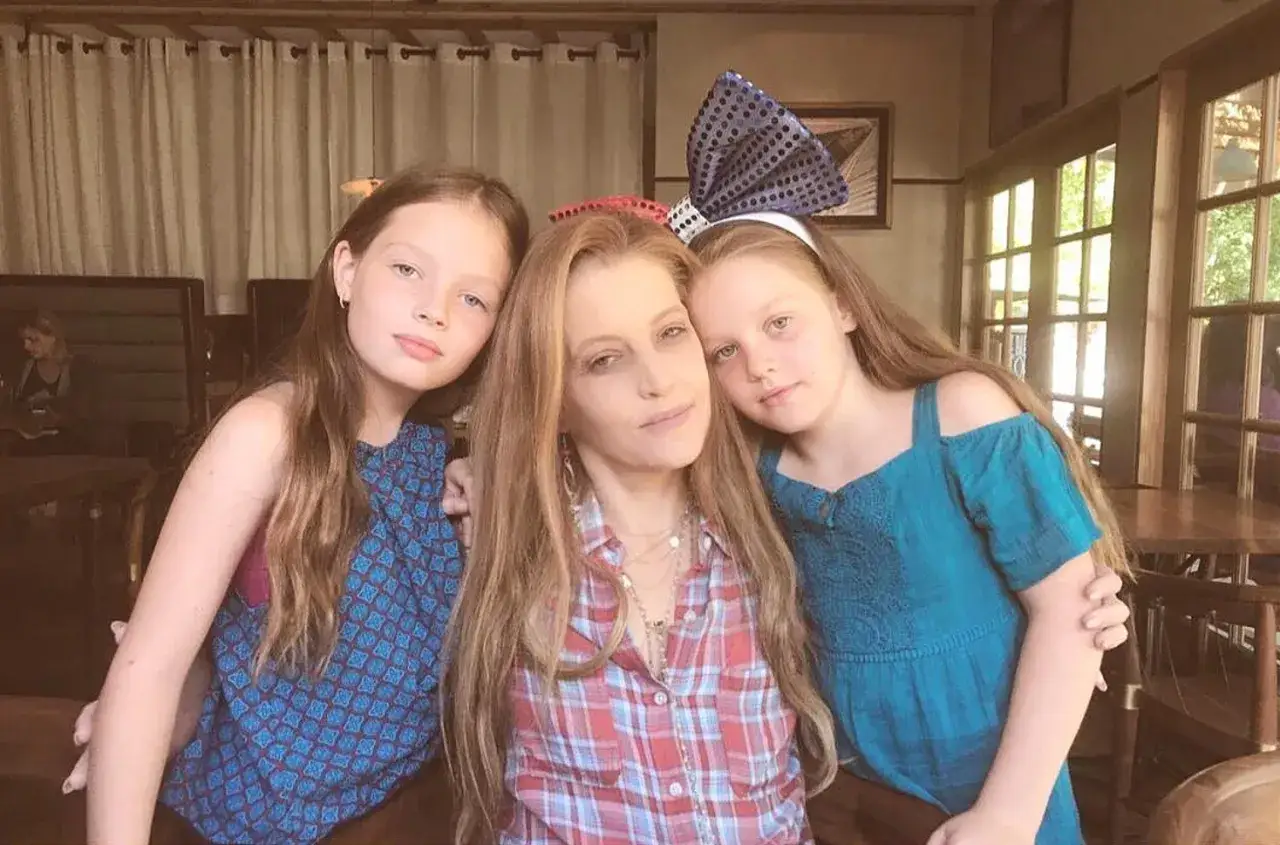 Lisa Marie Presley con le sue figlie, un tenero abbraccio tra madre e figlie, con una delle bambine che indossa un fiocco a pois.