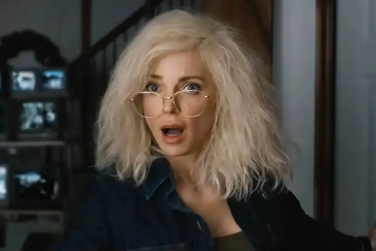 Kobieta z blond włosami i okularami, przerażona, jakby oglądała straszny film 6. W tle monitory.