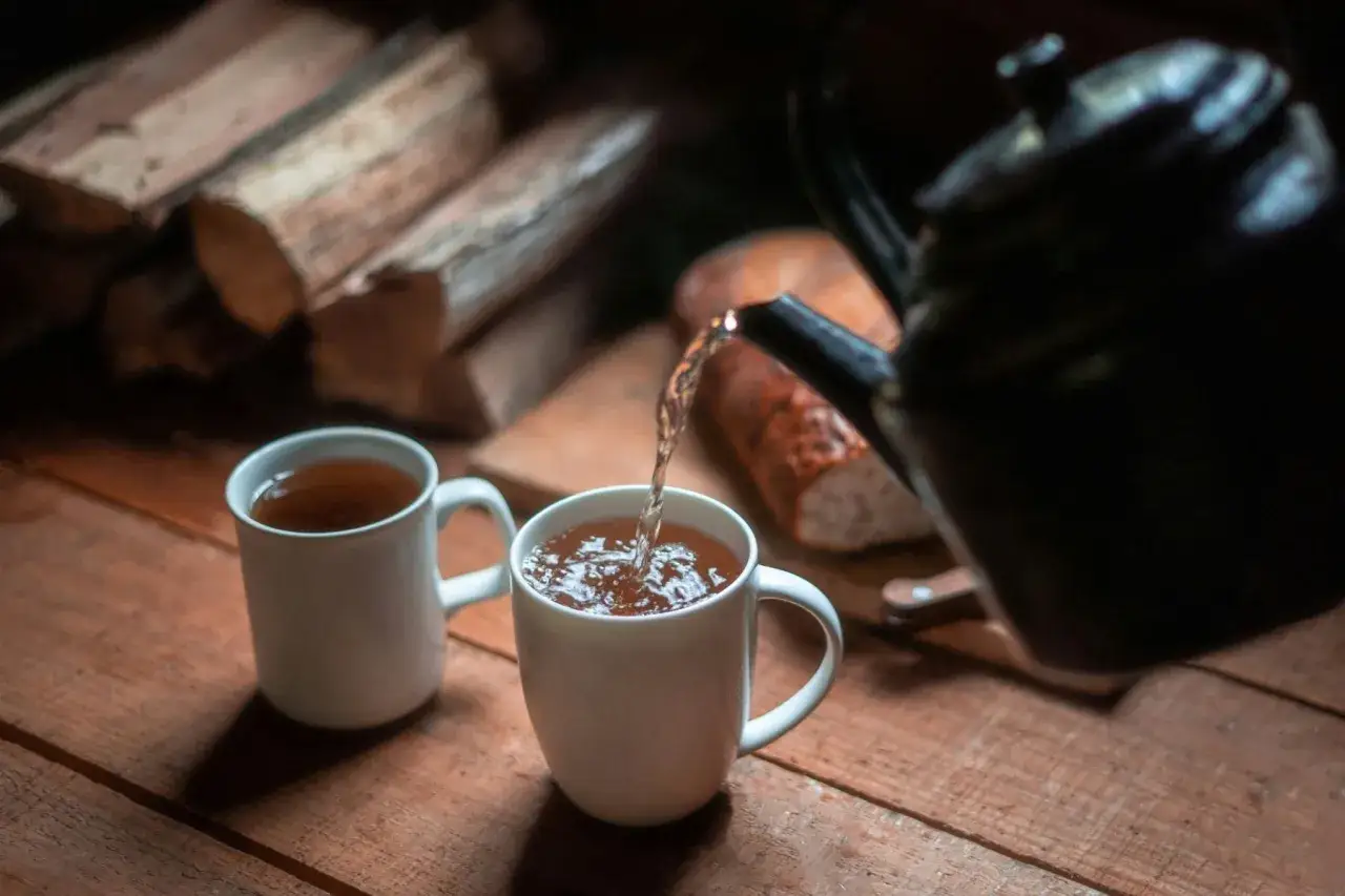 Un th&eacute; noir le soir, vers&eacute; dans une tasse blanche, avec du bois de chauffage en arri&egrave;re-plan.