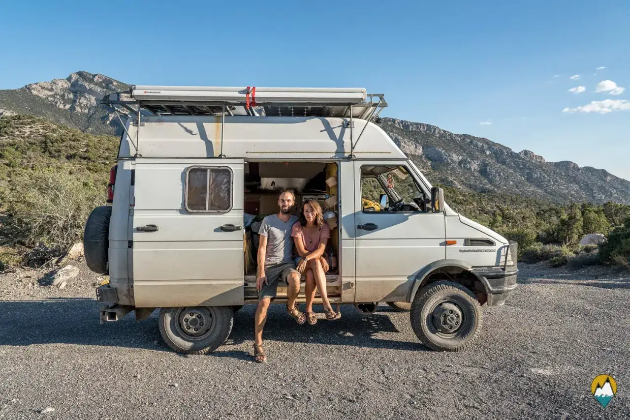 Couple assis à l'entrée d'un fourgon aménagé, prêt pour l'aventure. Ce véhicule est l'un des fourgons aménagés les plus fiables pour explorer les grands espaces.
