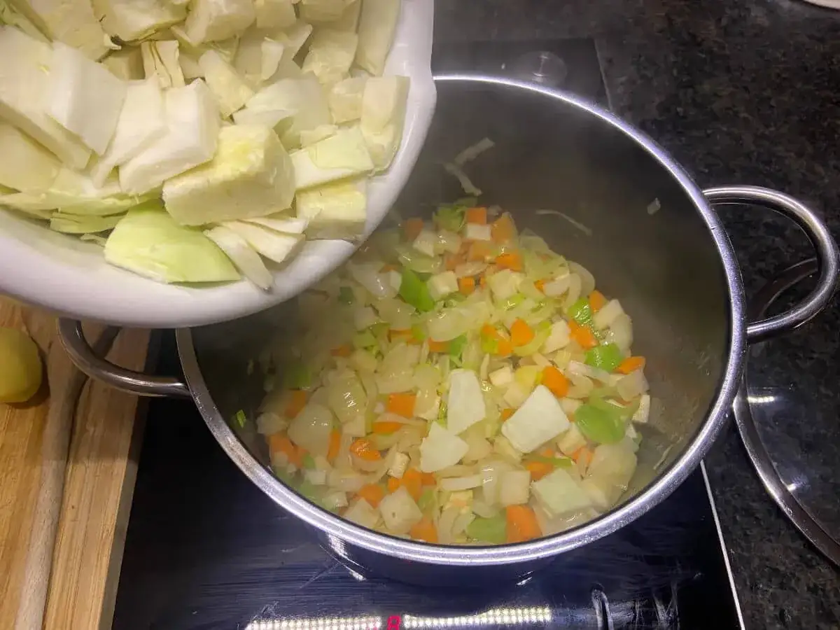 Kohl wird in einen Topf mit Gemüse gegeben, bereit für ein leckeres Kohlsuppe Rezept.