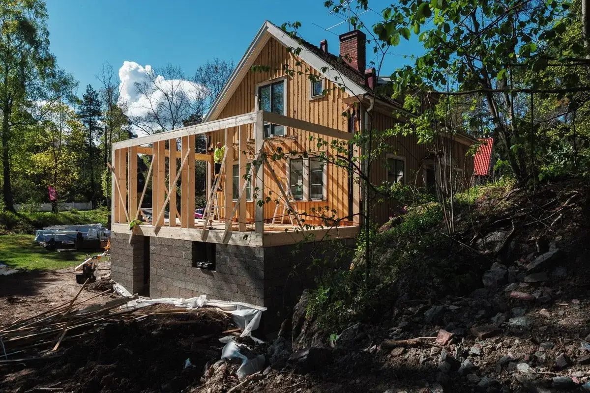 Husbyggnation i skogen. En ny stomme byggs på ett befintligt hus. Frågan