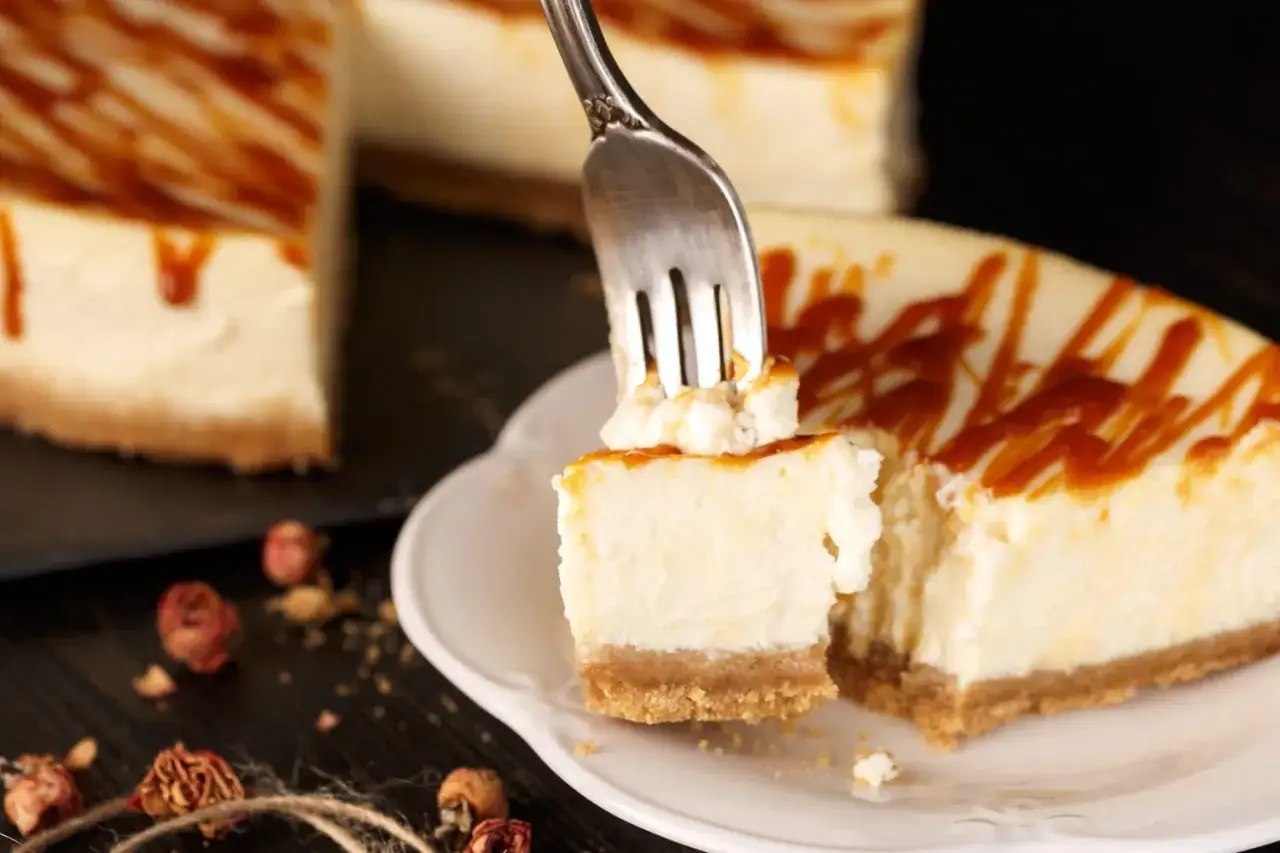 Une fourchette pr&eacute;l&egrave;ve un morceau d'un cheesecake cr&eacute;meux, garni de sauce caramel. Le fromage frais pour cheesecake est parfait pour cette gourmandise.
