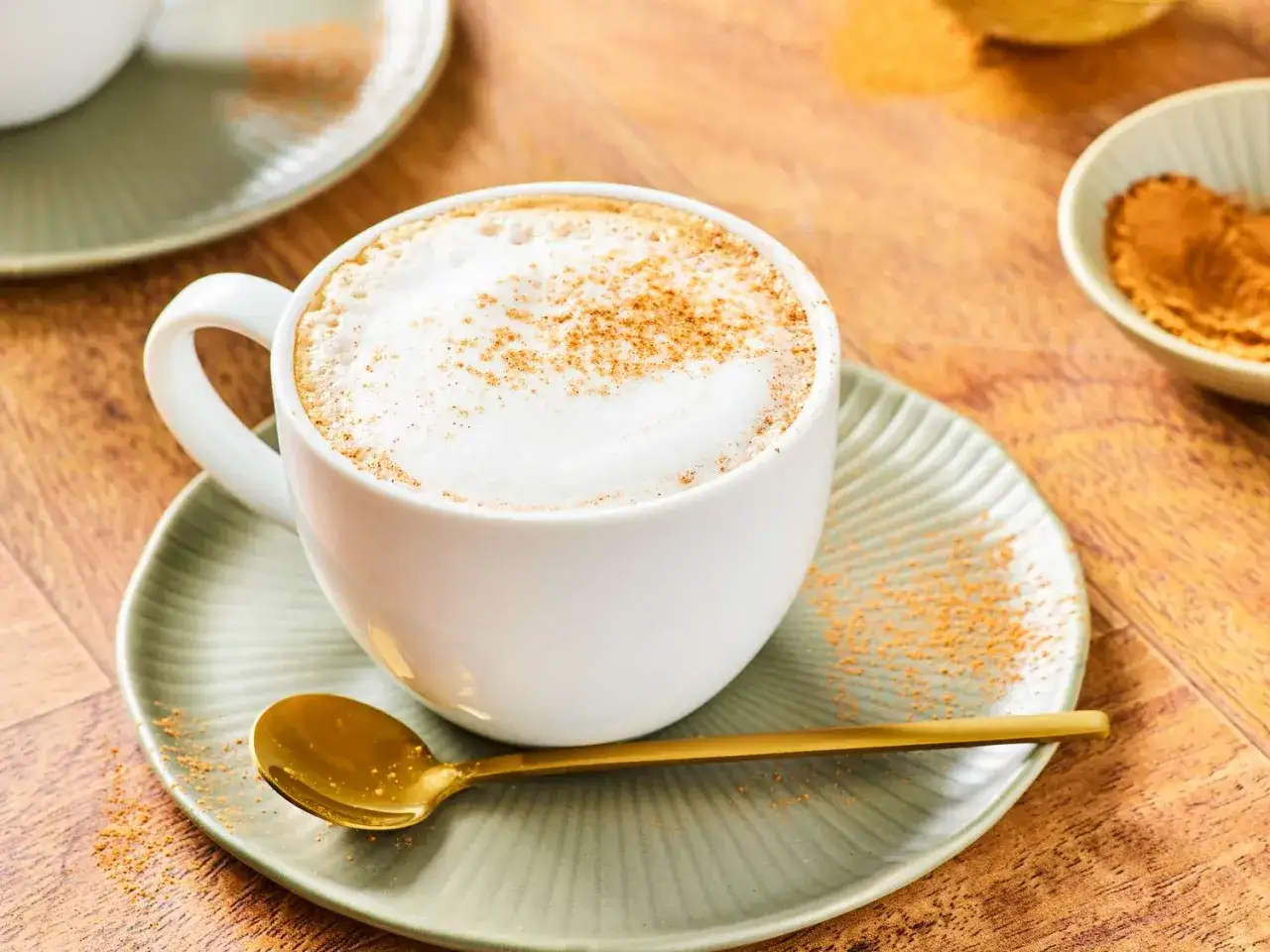 Aksamitne cappuccino posypane cynamonem. Czy cappuccino jest zdrowe? Złota łyżeczka czeka na pierwszy łyk.