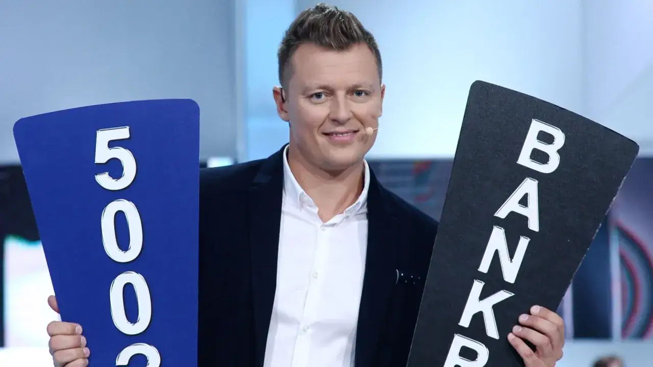 Rafał Brzozowski, znany z teleturniejów, trzyma tabliczki z napisem