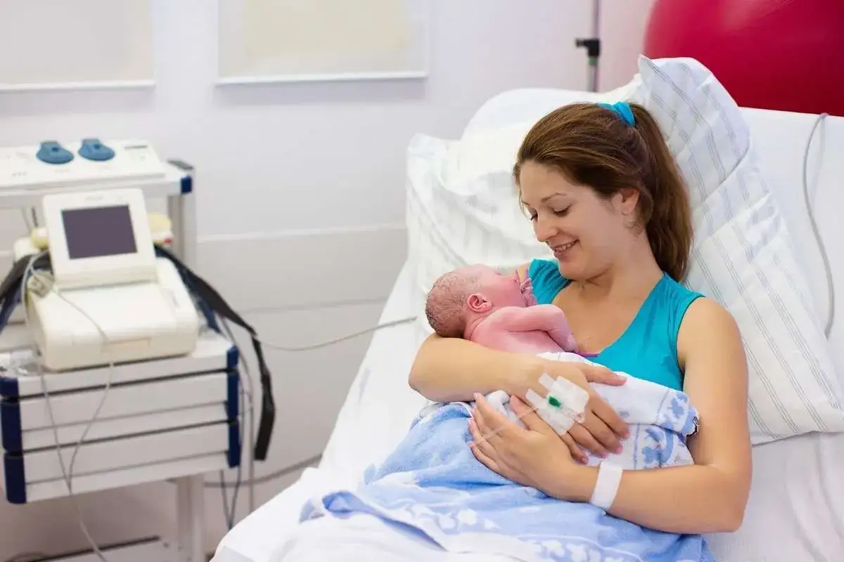 Szczęśliwa mama tuli noworodka po porodzie. Obok stoi aparat KTG, monitorujący stan dziecka.