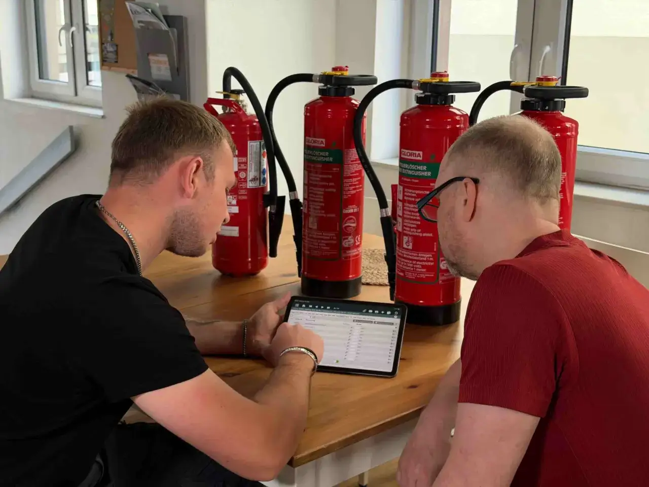 Zwei Männer prüfen mit einem Tablet die Daten von Feuerlöschern. Die regelmäßige **Wandhydranten Wartung** ist entscheidend für die Sicherheit.