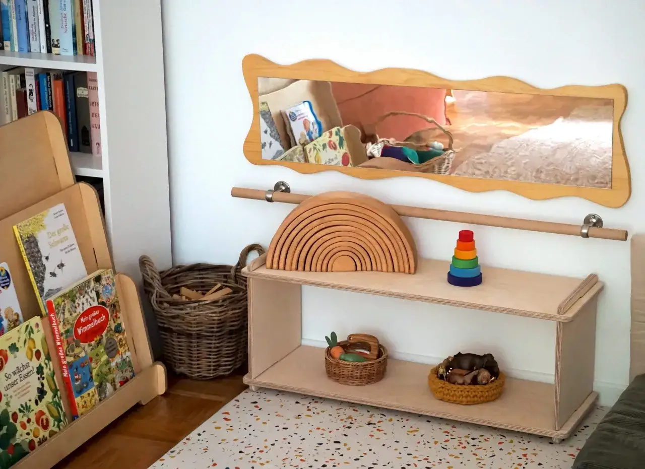 Ein helles, freundliches Montessori Kinderzimmer mit Holzspielzeug, Büchern und Körben. Ein Regenbogen aus Holz und ein Stapelturm laden zum Spielen ein.