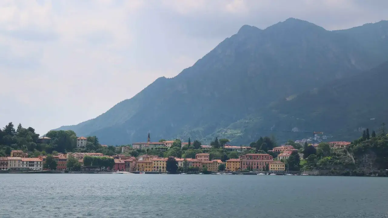 Färgglada hus längs en sjö vid foten av ett berg. En idyllisk vy över Lago Maggiore.