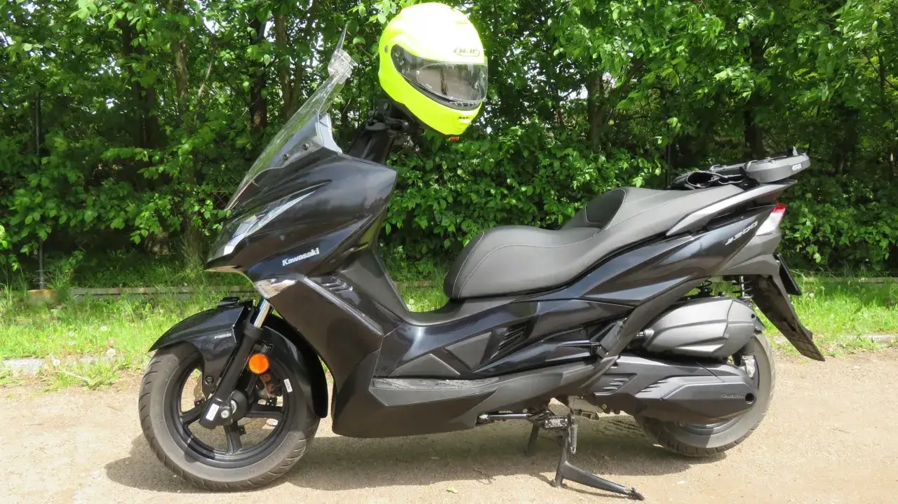 Czarny skuter Kawasaki J300 z jaskrawożółtym kaskiem na kierownicy, gotowy do jazdy pośród zieleni.
