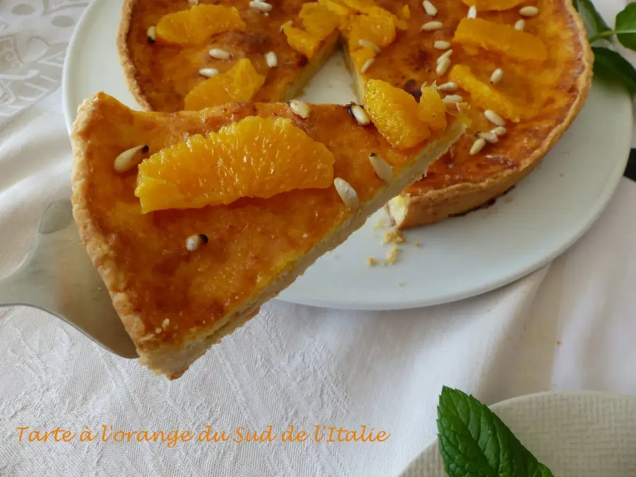 Une part de tarte à l'orange, garnie de quartiers d'orange et de pignons de pin, est servie sur une pelle à tarte.