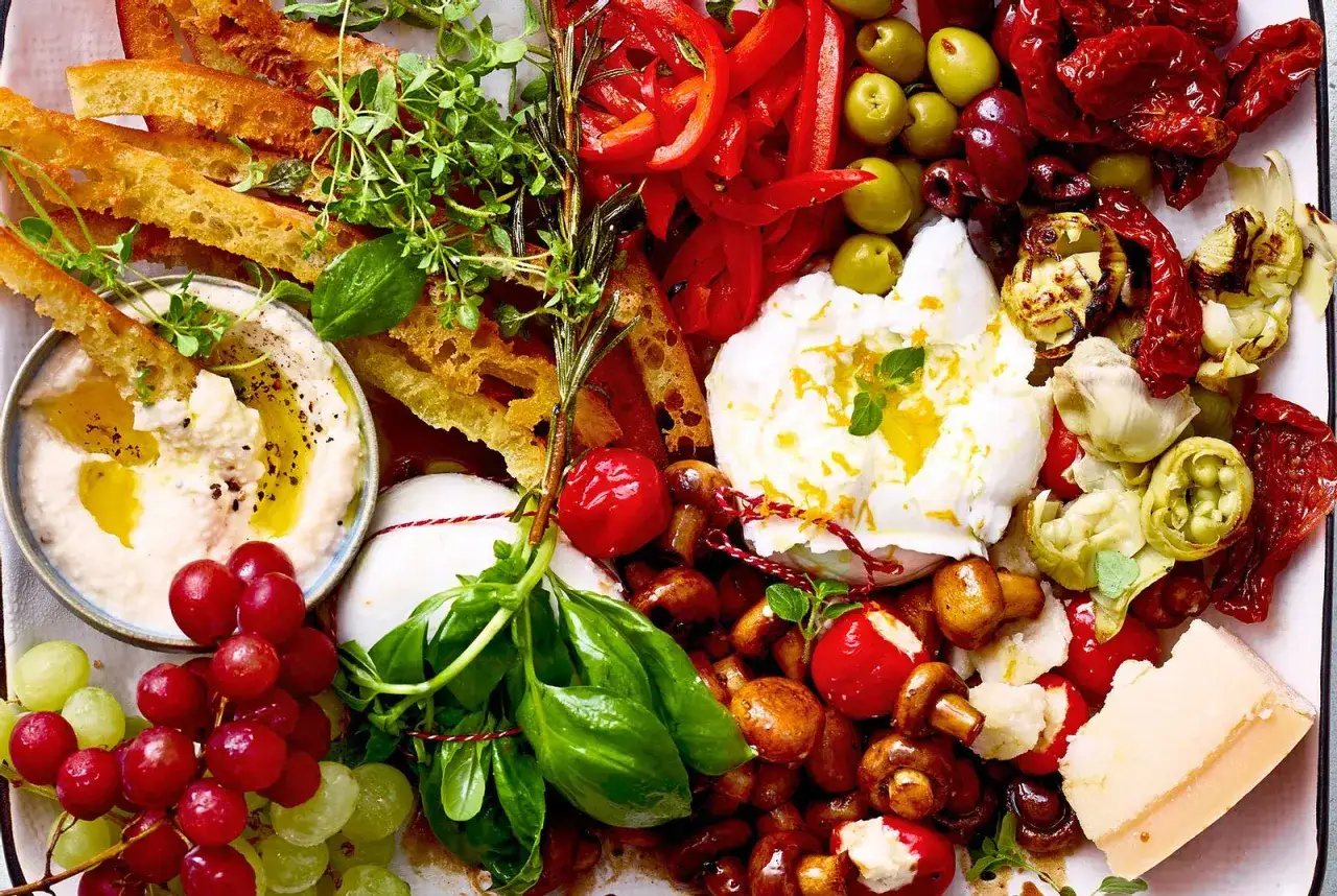 Antipasti selber machen: Köstliche Auswahl mit Hummus, Burrata, Trauben, Oliven, Pilzen, Paprika und Brot.