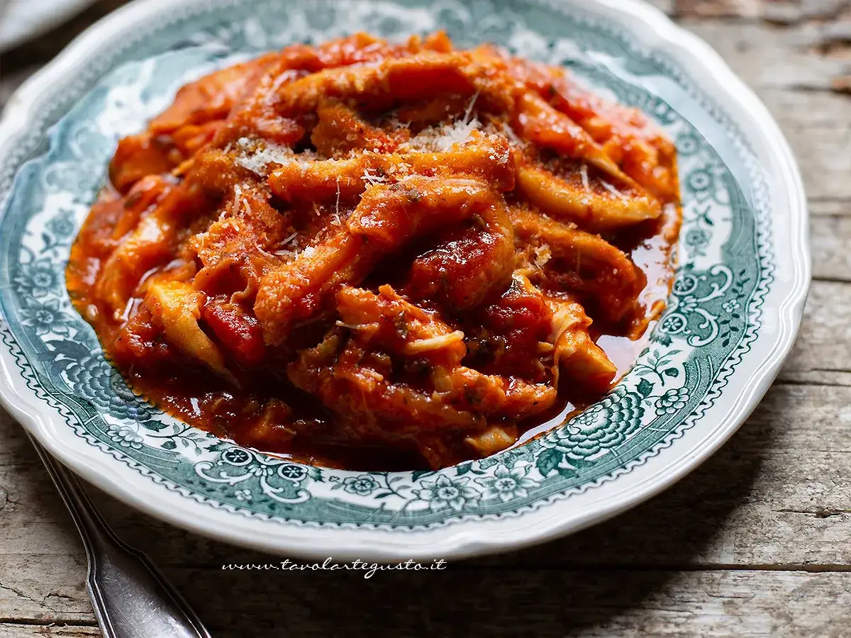 Un piatto fumante di trippa alla romana, ricca di sugo di pomodoro e pecorino, servita su un piatto decorato.
