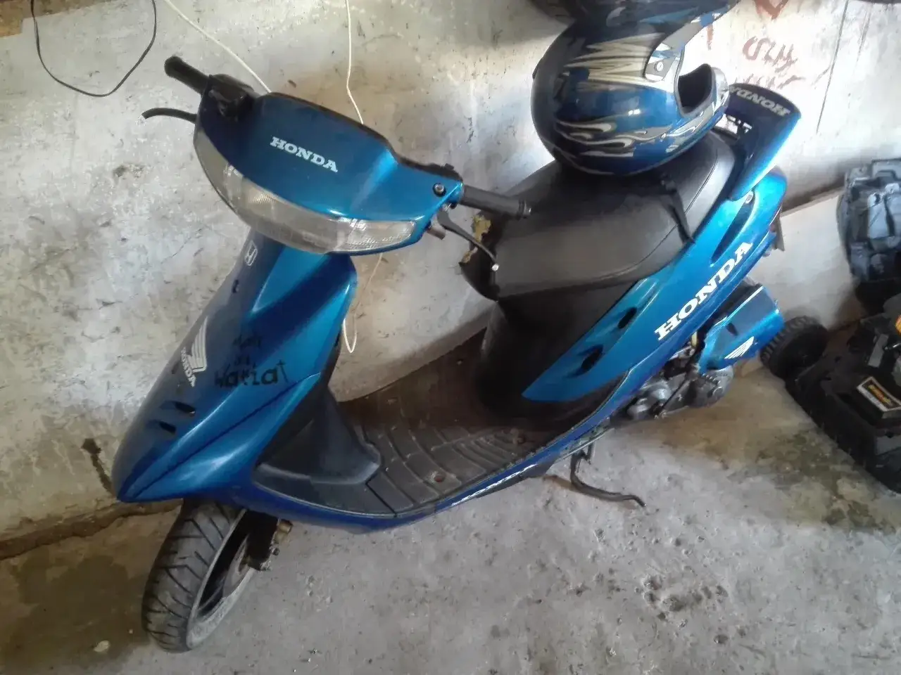Niebieski skuter Honda Dio z niebieskim kaskiem ozdobionym płomieniami.