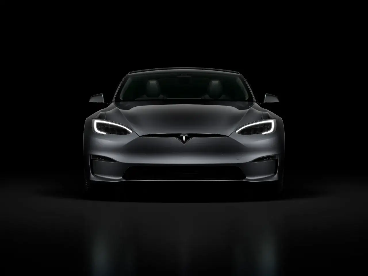 Szary Tesla Model S z włączonymi światłami, prezentujący nowoczesny design. Tesla co to? To przyszłość motoryzacji.