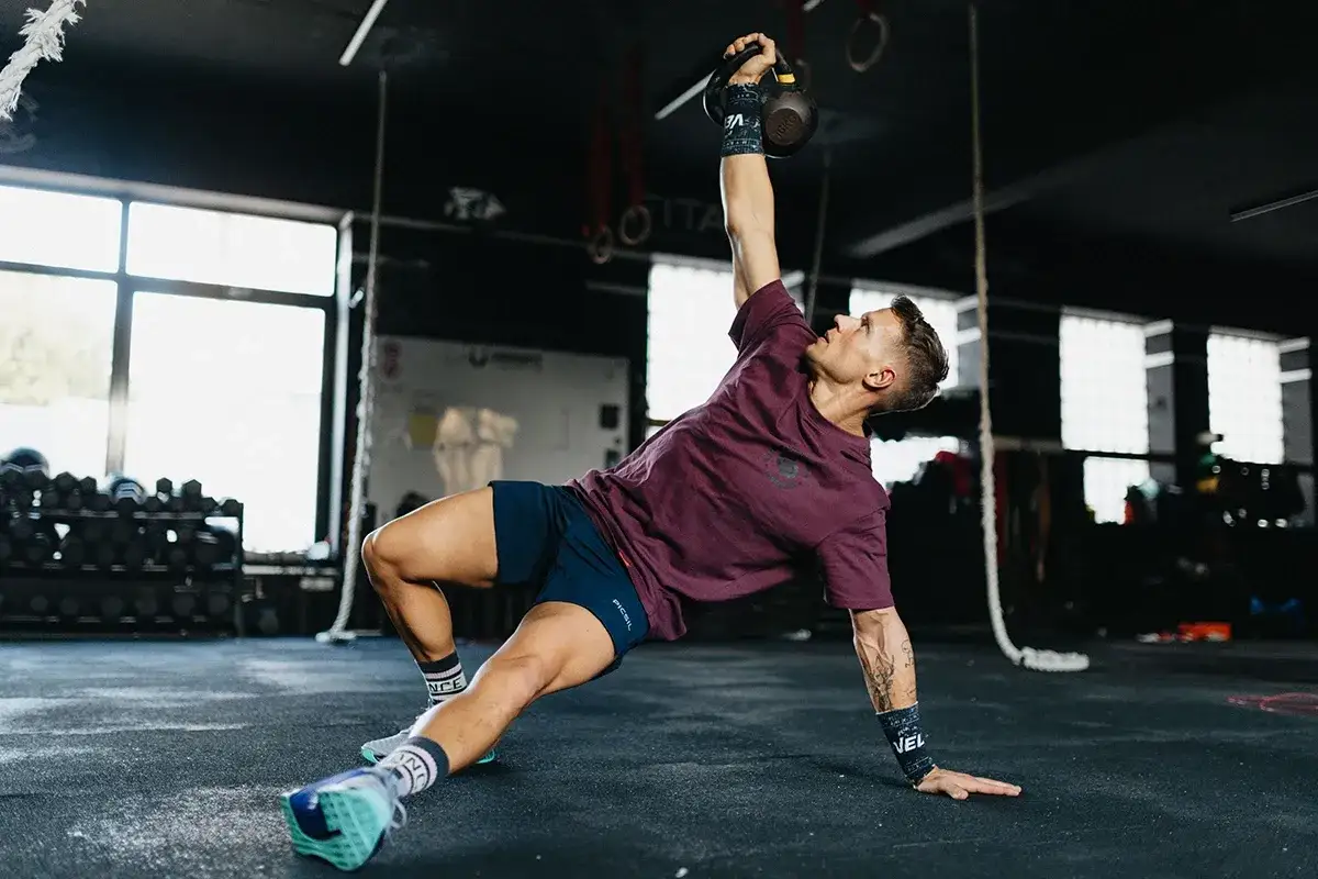 Mężczyzna wykonuje ćwiczenia na gibkość z kettlebell, balansując ciałem na podłodze.