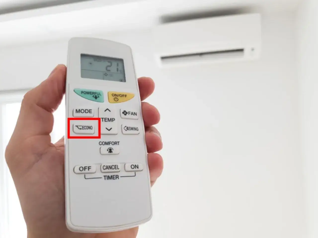 Mano sujetando un mando a distancia de aire acondicionado, con el botón