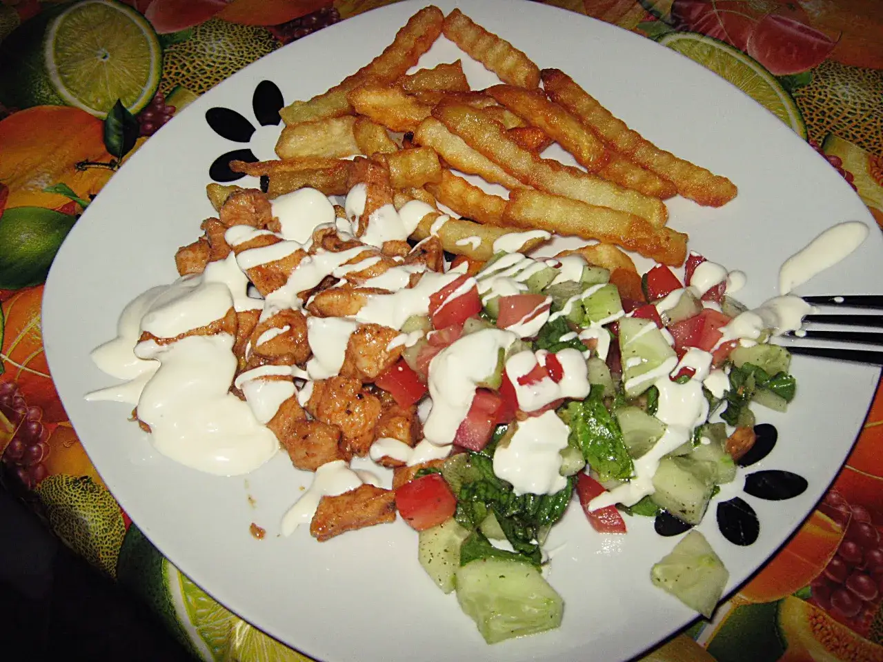 Pyszny kebab na talerzu z chrupiącymi frytkami i świeżą sałatką, polany kremowym sosem.